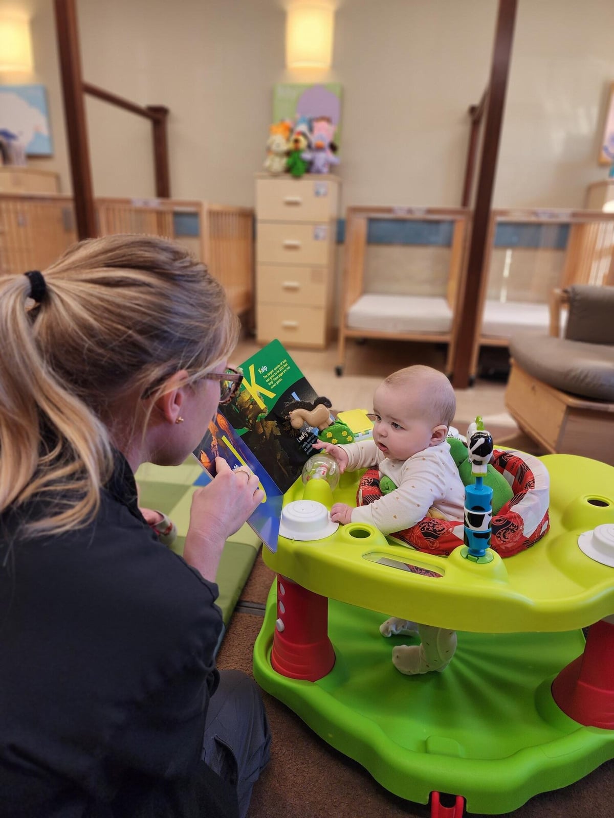 Infant teacher reading the ABC book to one infant and pointing out the characters. 