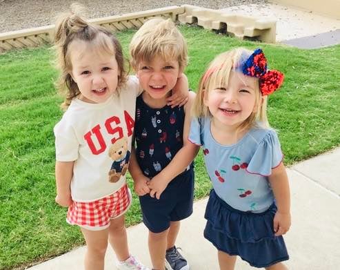 three early preschool children posing together in red white and blue patriotic fourth of july outfits on the playground of the best preschool pre-k daycare school near me, in fort worth saginaw texas 