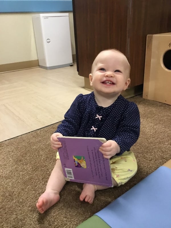 Smiling baby exploring a book in our Infant classroom