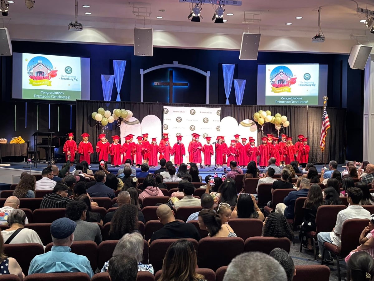 children in red graduation caps and gowns on stage 
