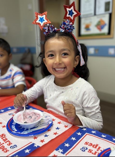 Smiling child celebrating the fourth of July during her classroom party eating a festive snack