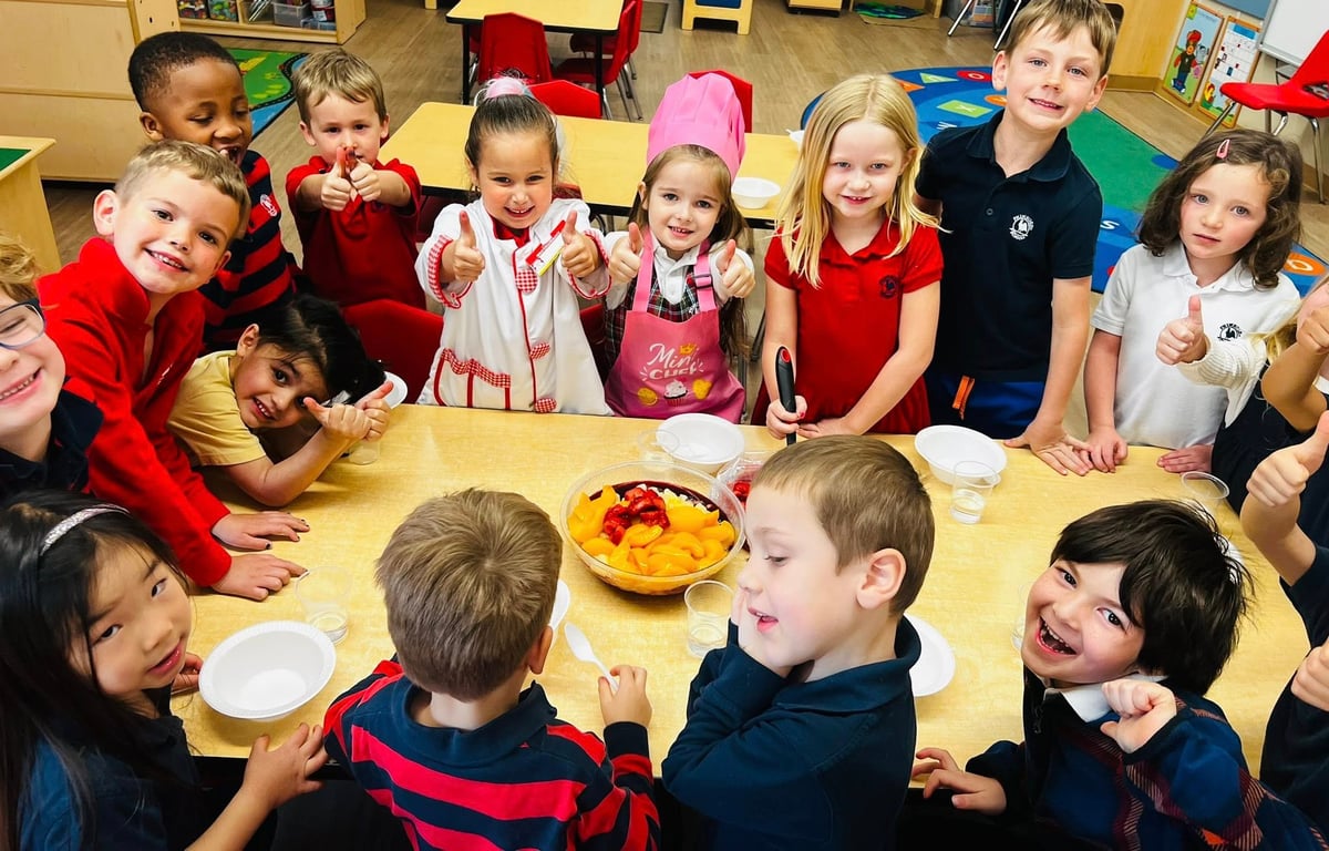 children in red, white, and blue school uniforms smiling as they pose with a fruit salad and bowls