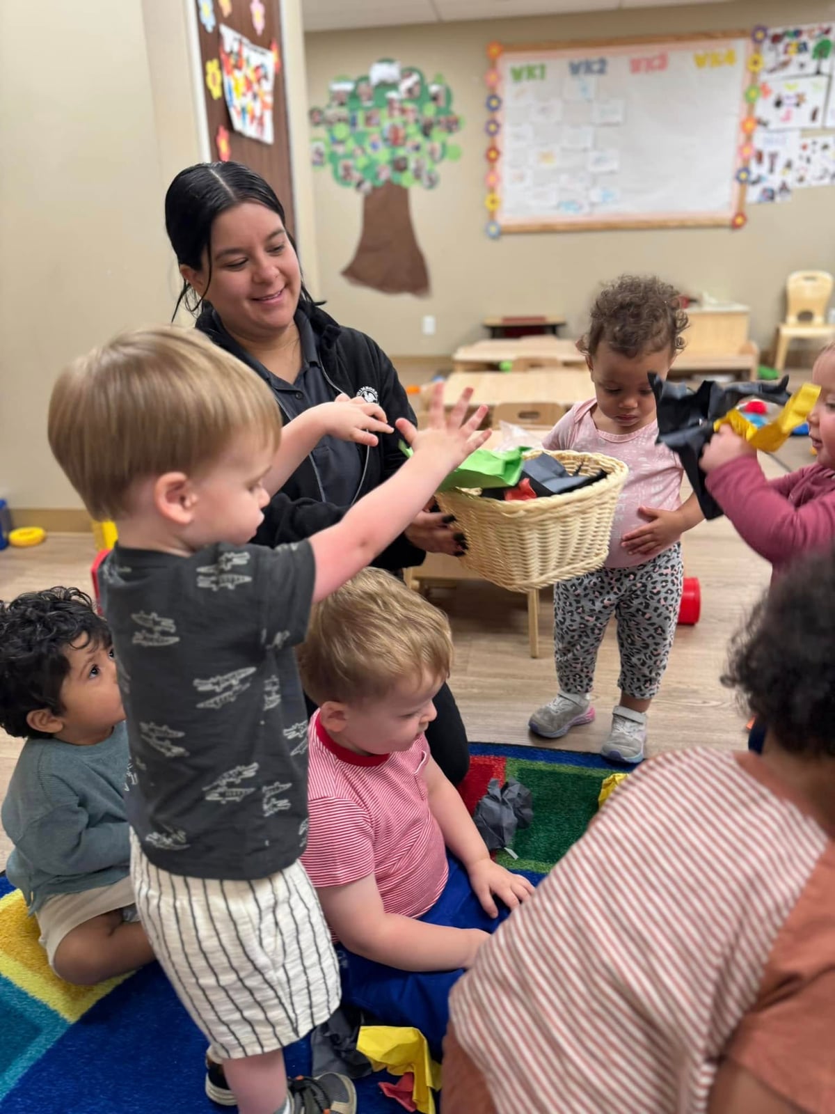 children helping their teacher sort toys into a basket