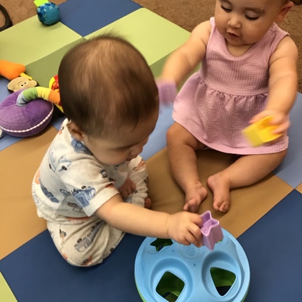 Two infants playing with shapes trying to place them into the matching shape. 