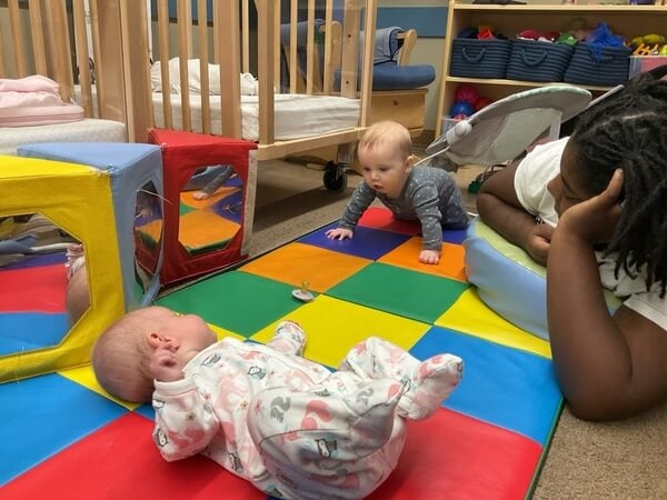 infants spend time with their teacher on the mat practicing tummy time and rolling over