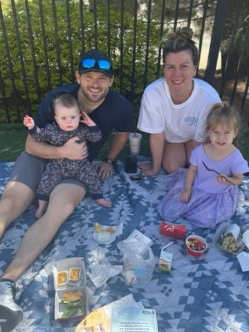 A family smiling while sitting on a picnic blanket enjoying lunch
