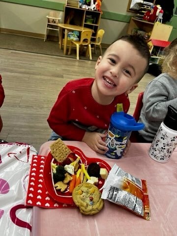 A child smiling with a red plate full of healthy snacks and red napkin decorated with hearts 