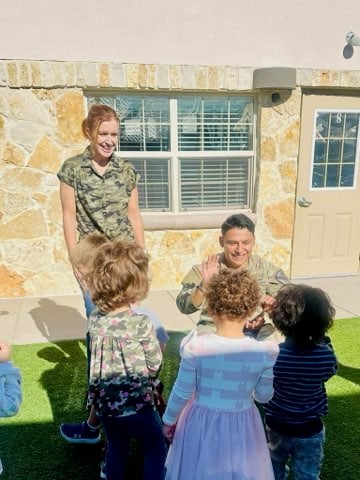 Three children on a playground giving high fives to a military service member in uniform