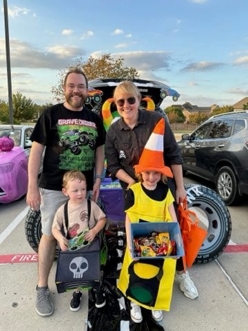 A family dressed up for Halloween, standing in front of their car, decorated for a Trunk-or-Treat celebration