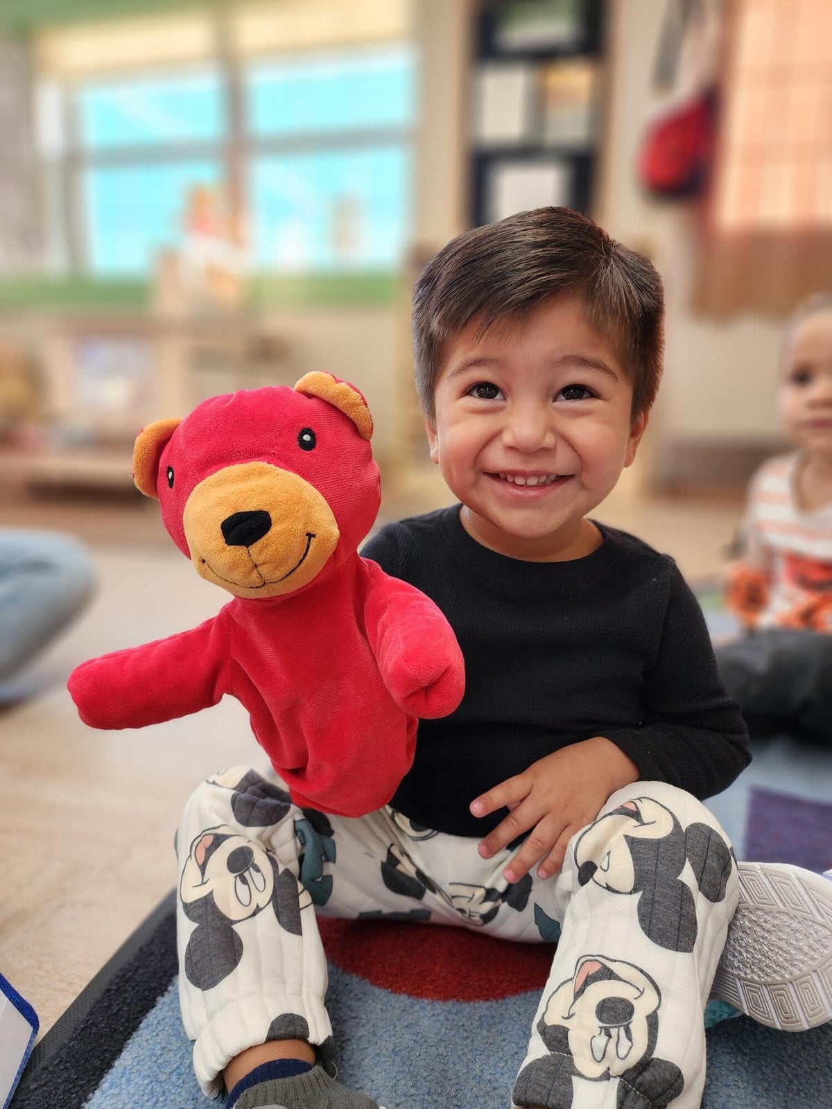 Smiling preschool student holding a classroom puppet during an early imaginative learning activity