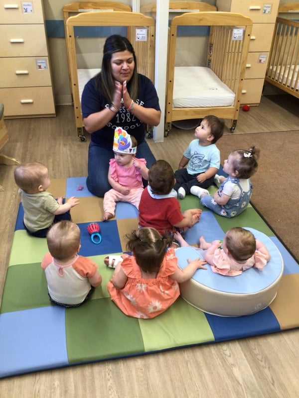 Infants sitting on a soft mat while teacher conducts music time. Happy and nurturing infant environment Heritage Trace Parkway.