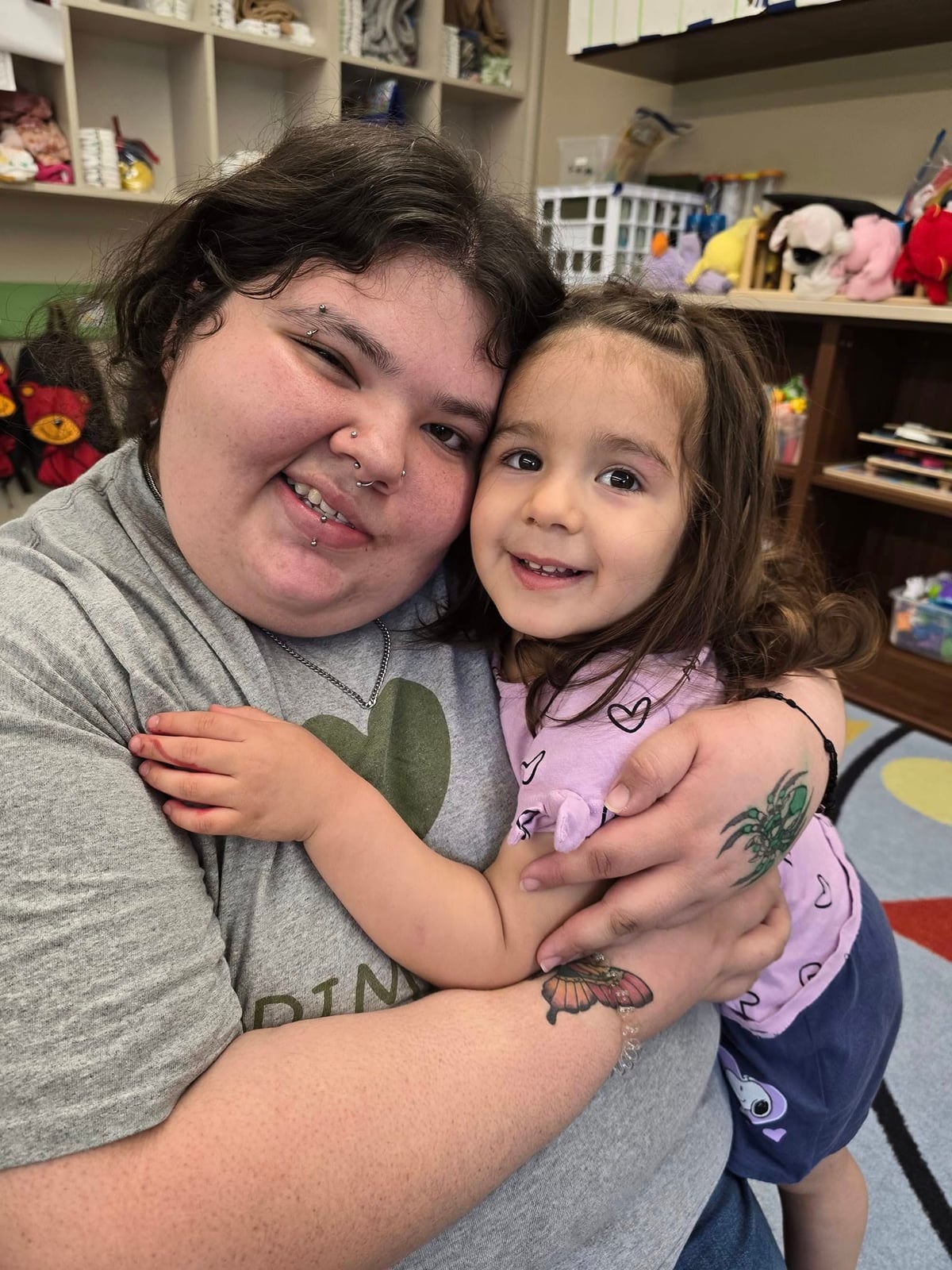 Teacher hugs smiling preschooler in classroom reading corner to support emotional development and early literacy skills