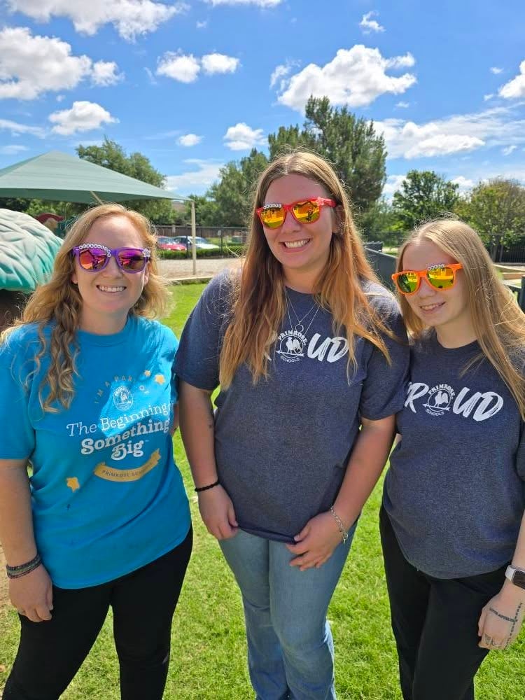 Three smiling staff wearing sunglasses and spirit shirts at outdoor school event, promoting community engagement in Keller,TX