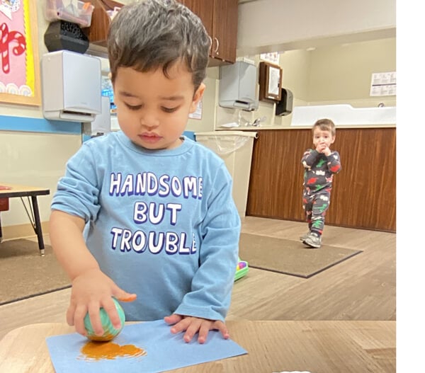 child in blue shirt using ball to paint