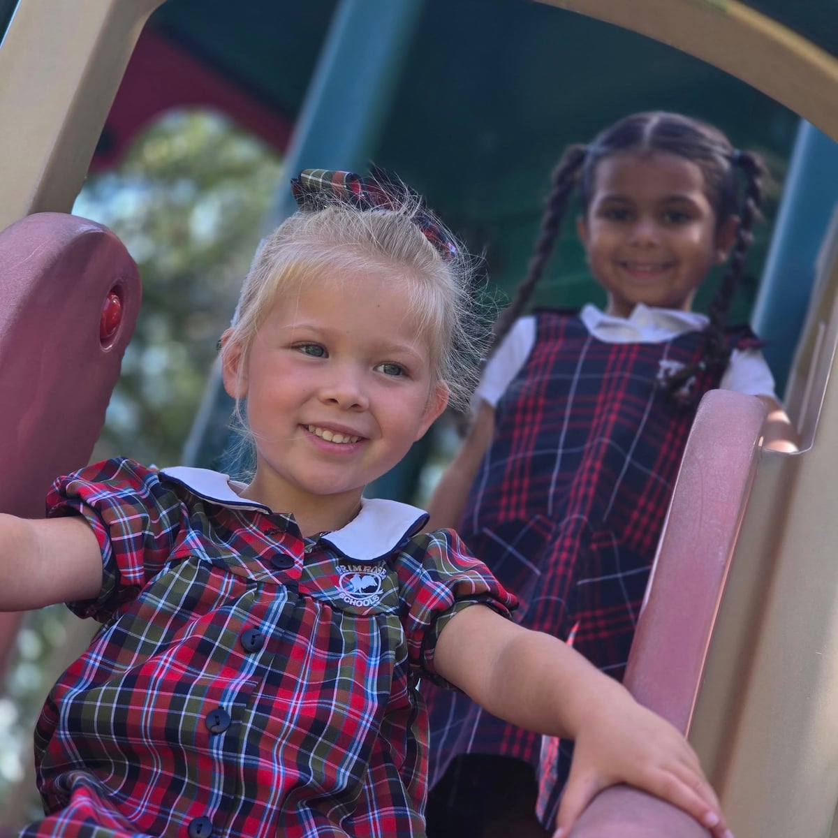 two girls in plaid dresses going down a slide