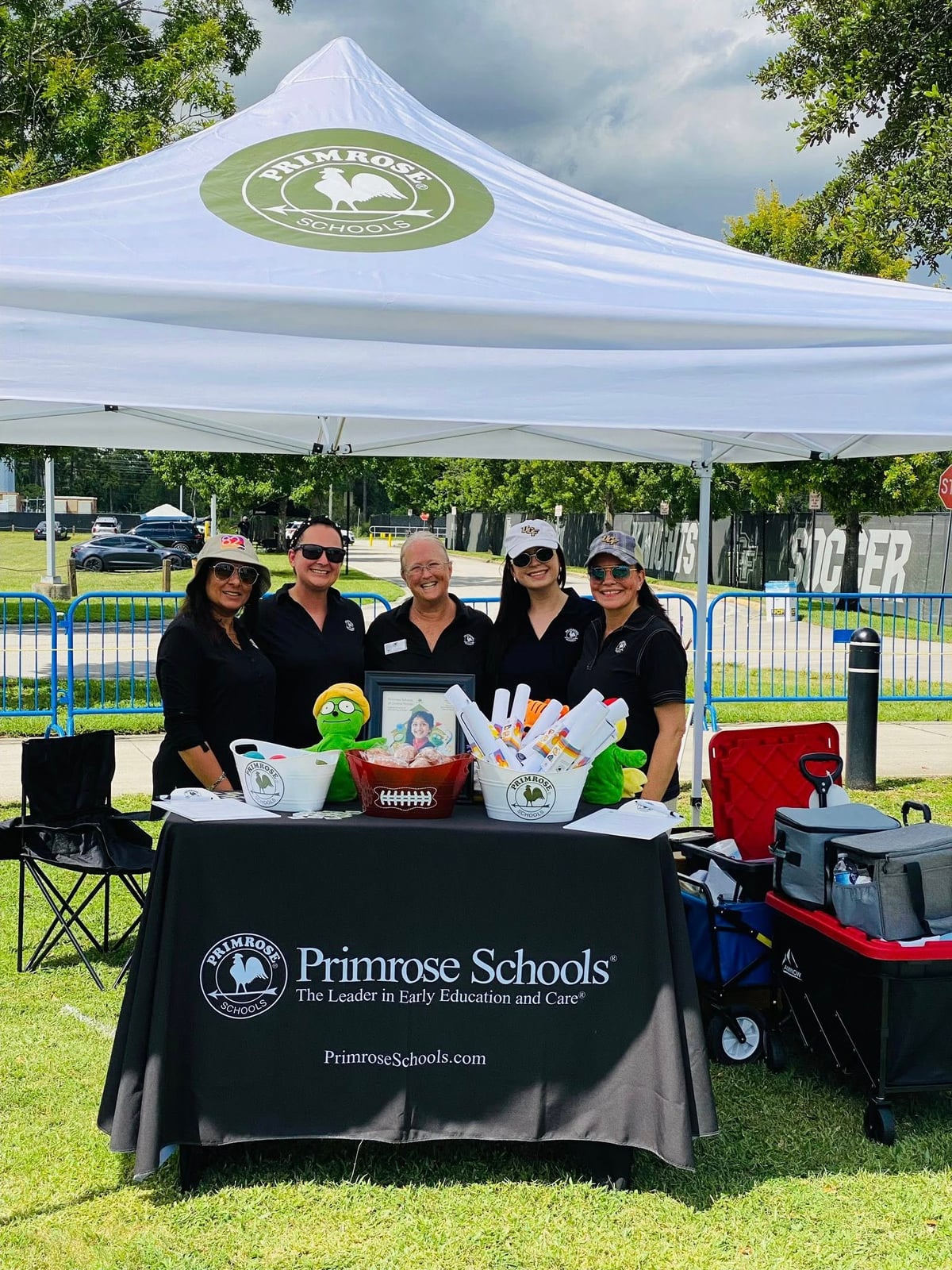 white tent with green primrose logo 5 women standing in grass behind a black tablecloth