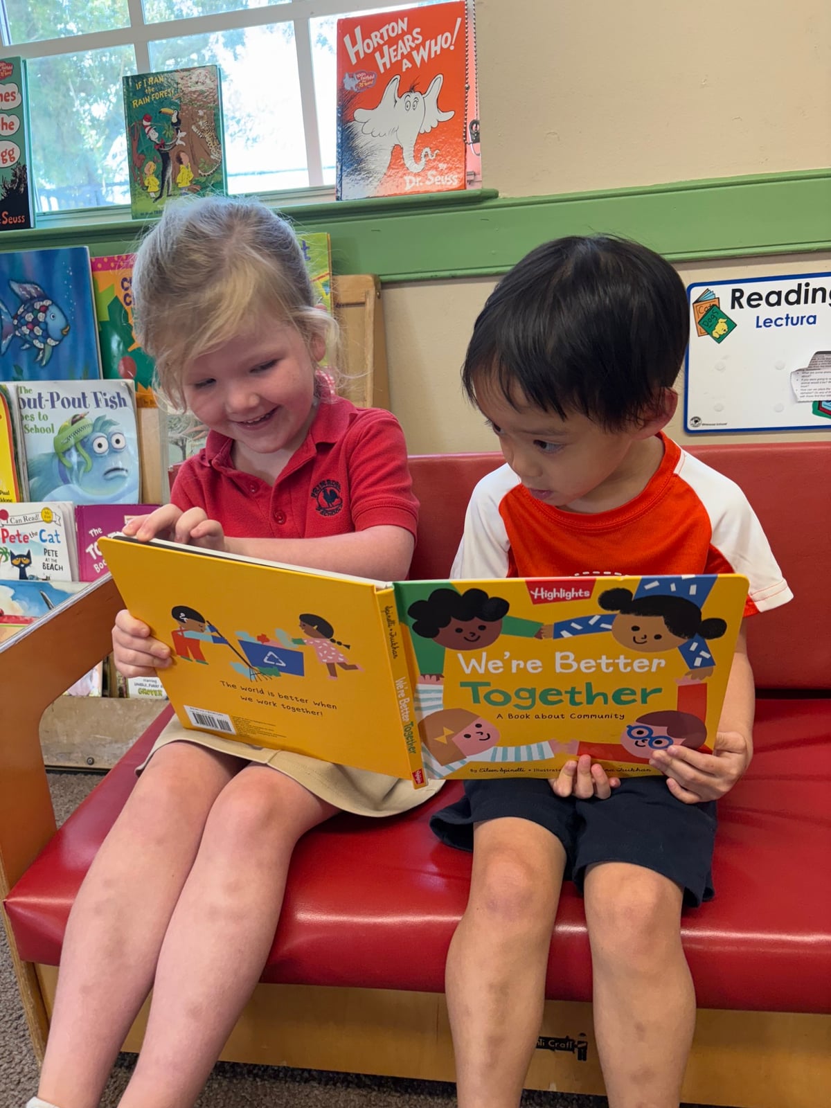 Two children sitting on a red couch holding a yellow book together that is titled "We're better together" with children on the front and back cover.