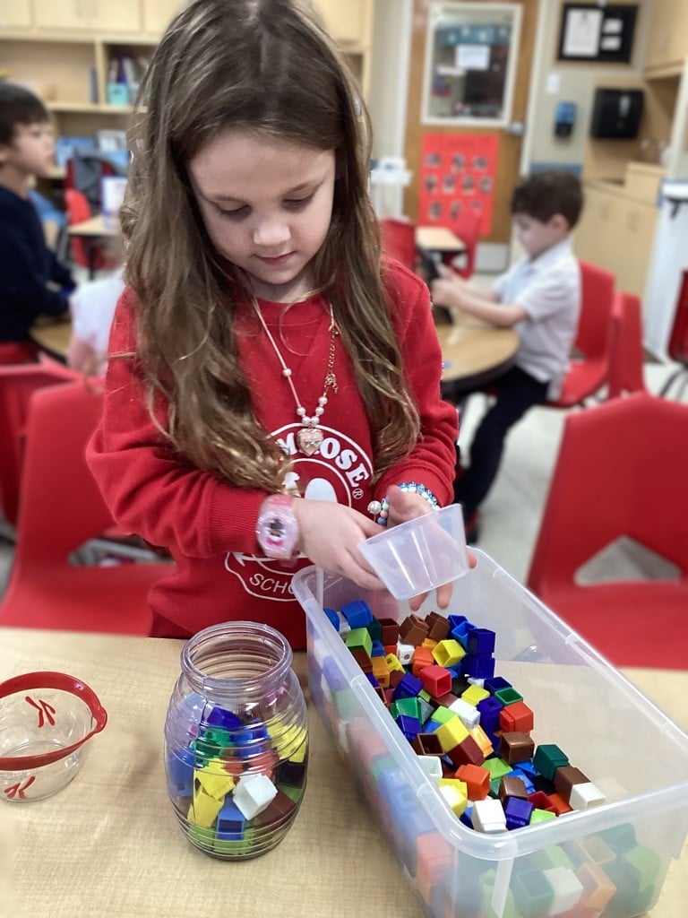 little girl placing colored cubes into a clear jar