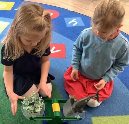 2 girls using a balance scale to compare the weight of 2 objects