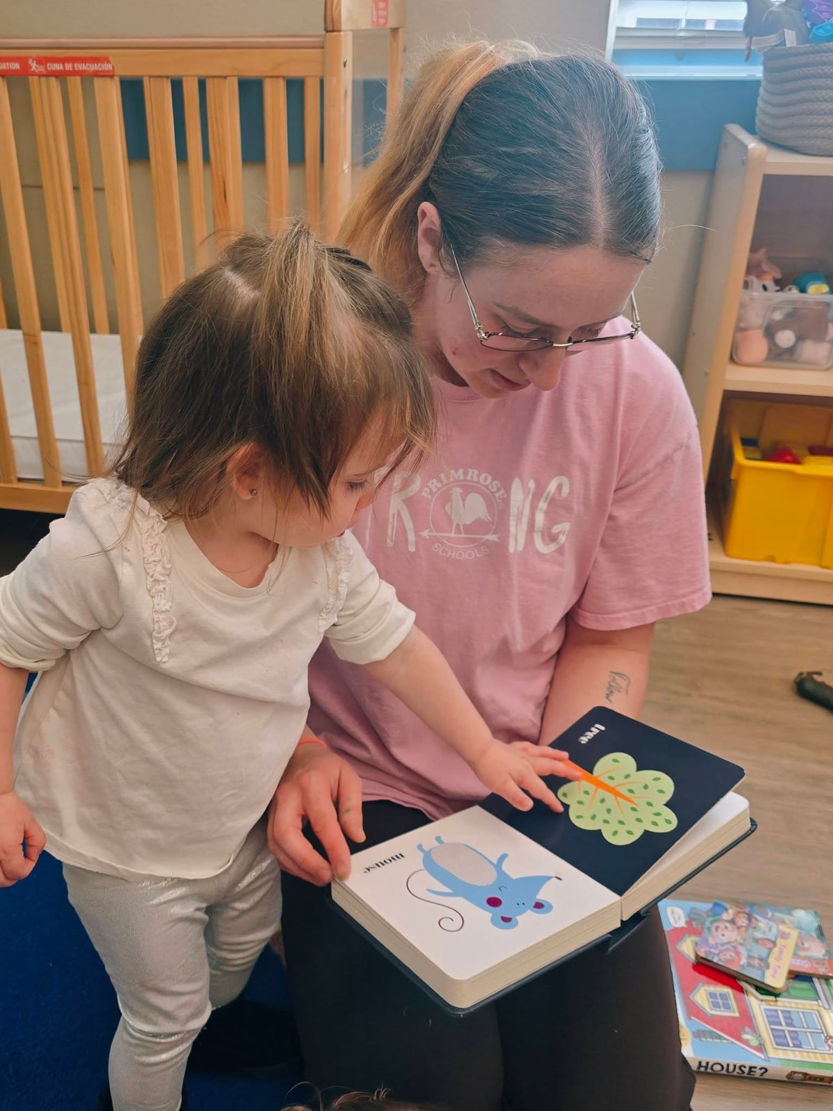 Teacher and toddler girl reading a book together in a daycare classroom in Keller, TX.