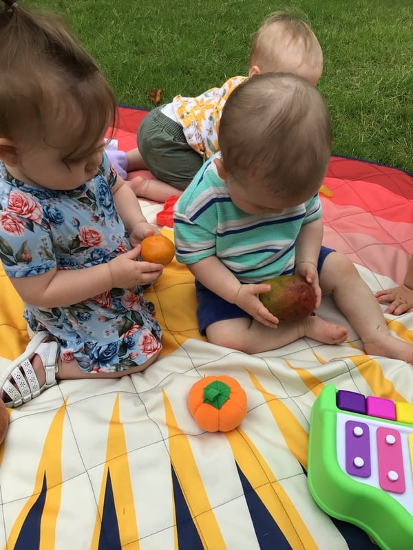3 Infants playing outside on a soft mat while exploring fruits and vegetables at the best childcare center in Keller, TX.