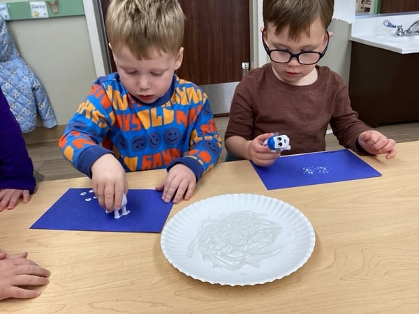 two children sitting at table with blue paper