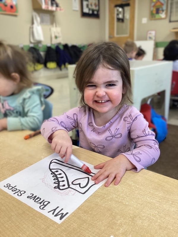 little girl smiling and coloring a shoe with a marker