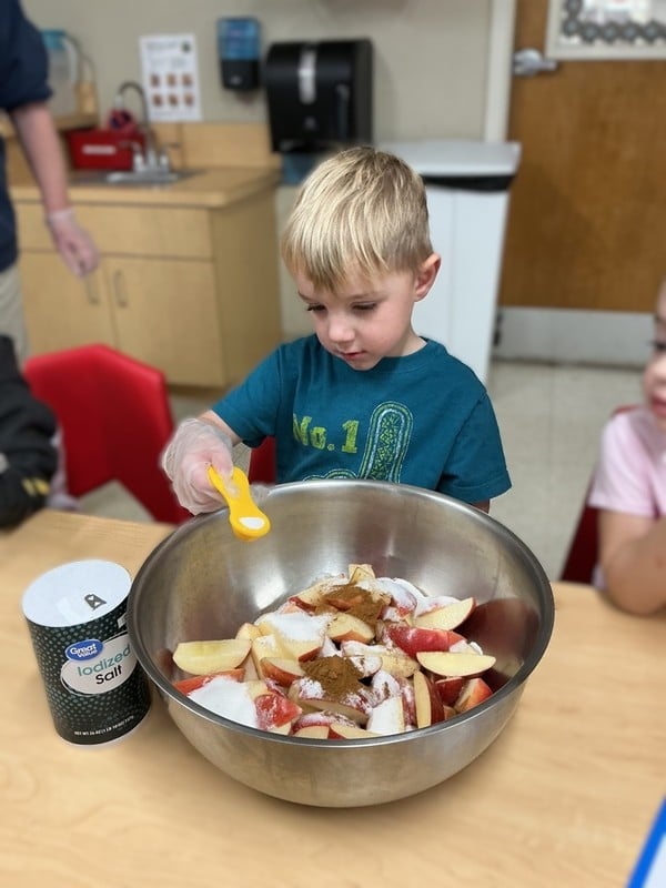 little boy adding ingredients to a bowl of food items