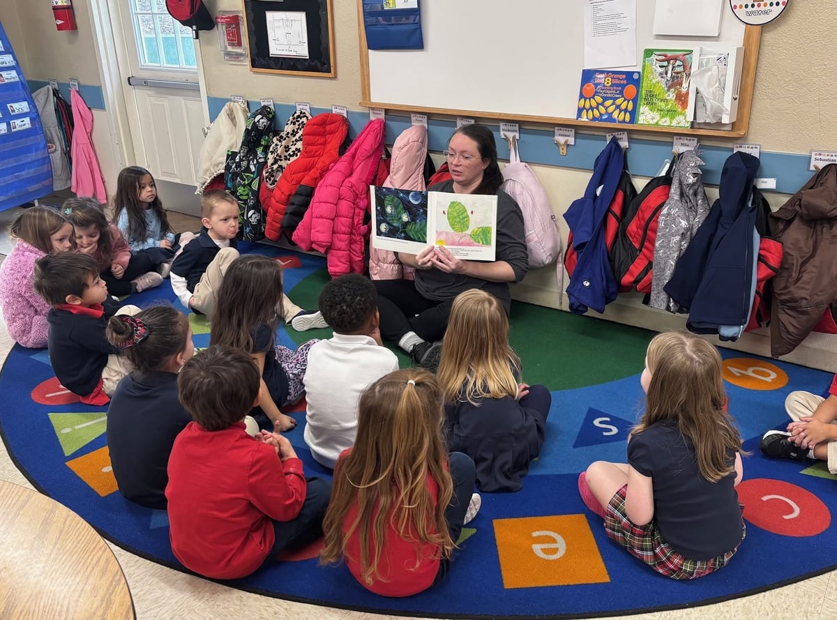 a group of children sitting on a carpet listening to a teacher read a book