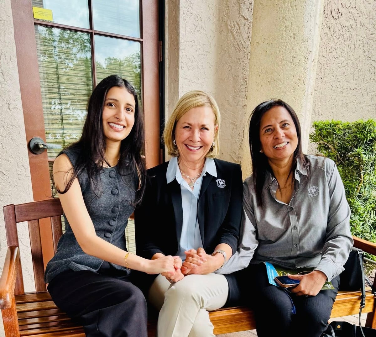 Primrose School CEO in the middle in blue shirt and black blazer with blonde hair, on the right woman with grey button down shirt and black hair, on the left woman with brown hair and grey button down all holding hands