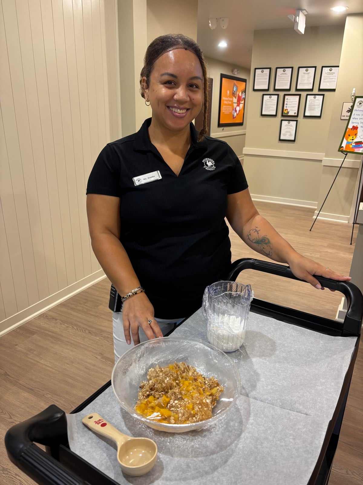 Teacher in black polo with name tag in front of black cart with peach crisp in a bowl and a container of milk