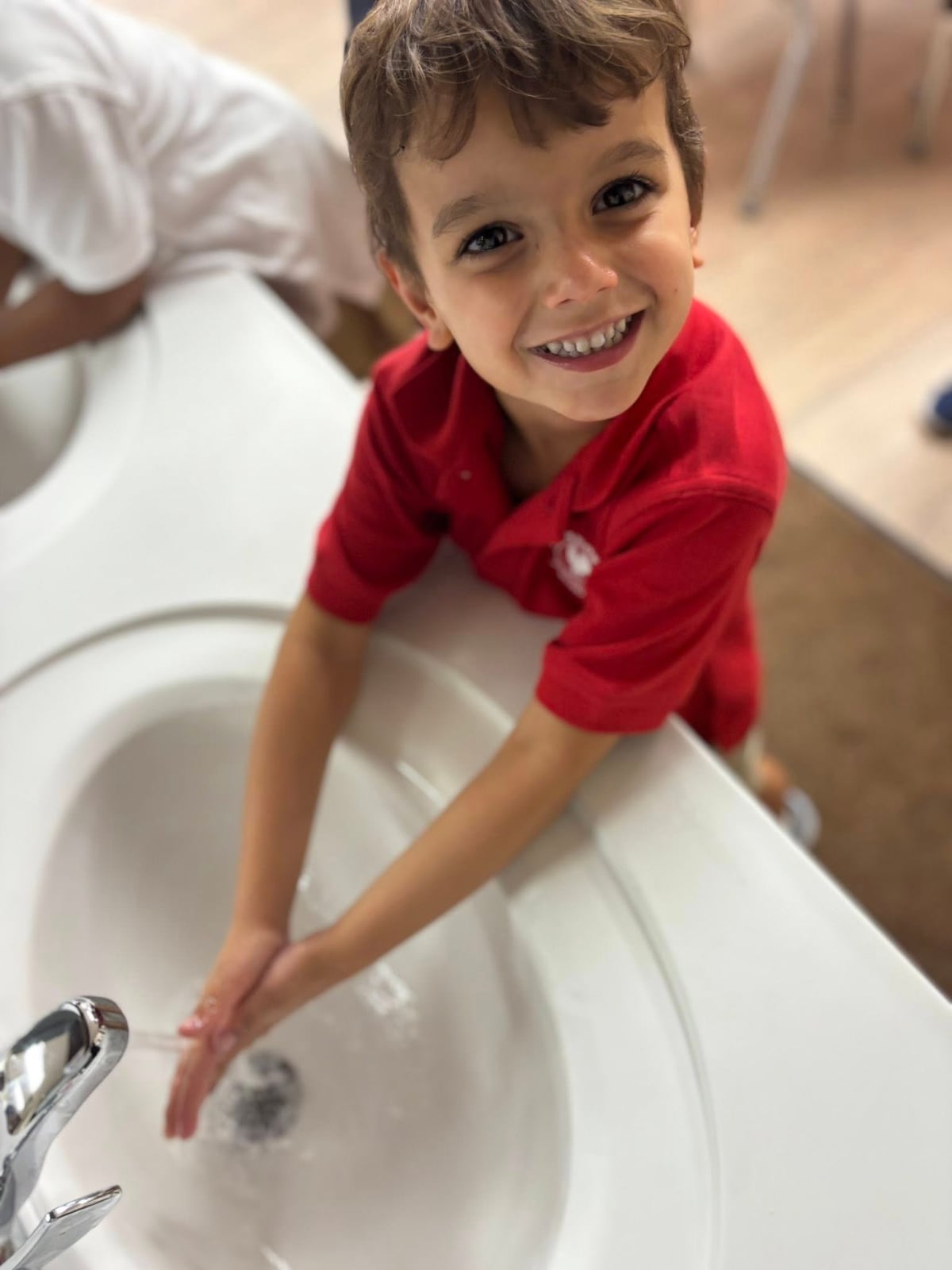 child in red shirt washing hands in a sink