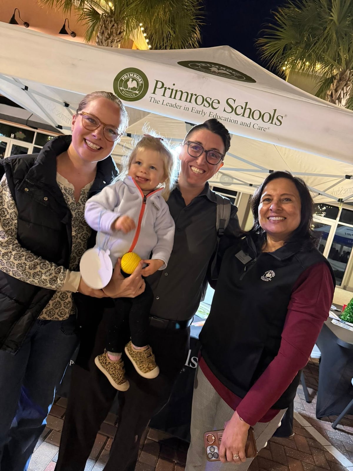 Three women and a toddler little girl in front of a Primrose white tent