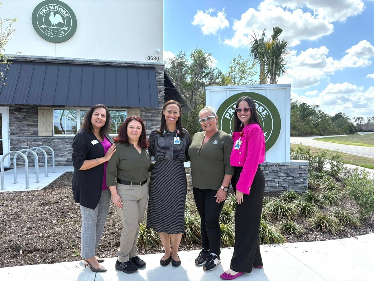 five women standing outside a building in front of a green primrose logo